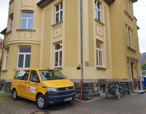 Der gelbe "Boni"-Bus steht vor den Außenwänden des Pfarrhauses, hinter denen sich das Pfarrbüro verbirgt.